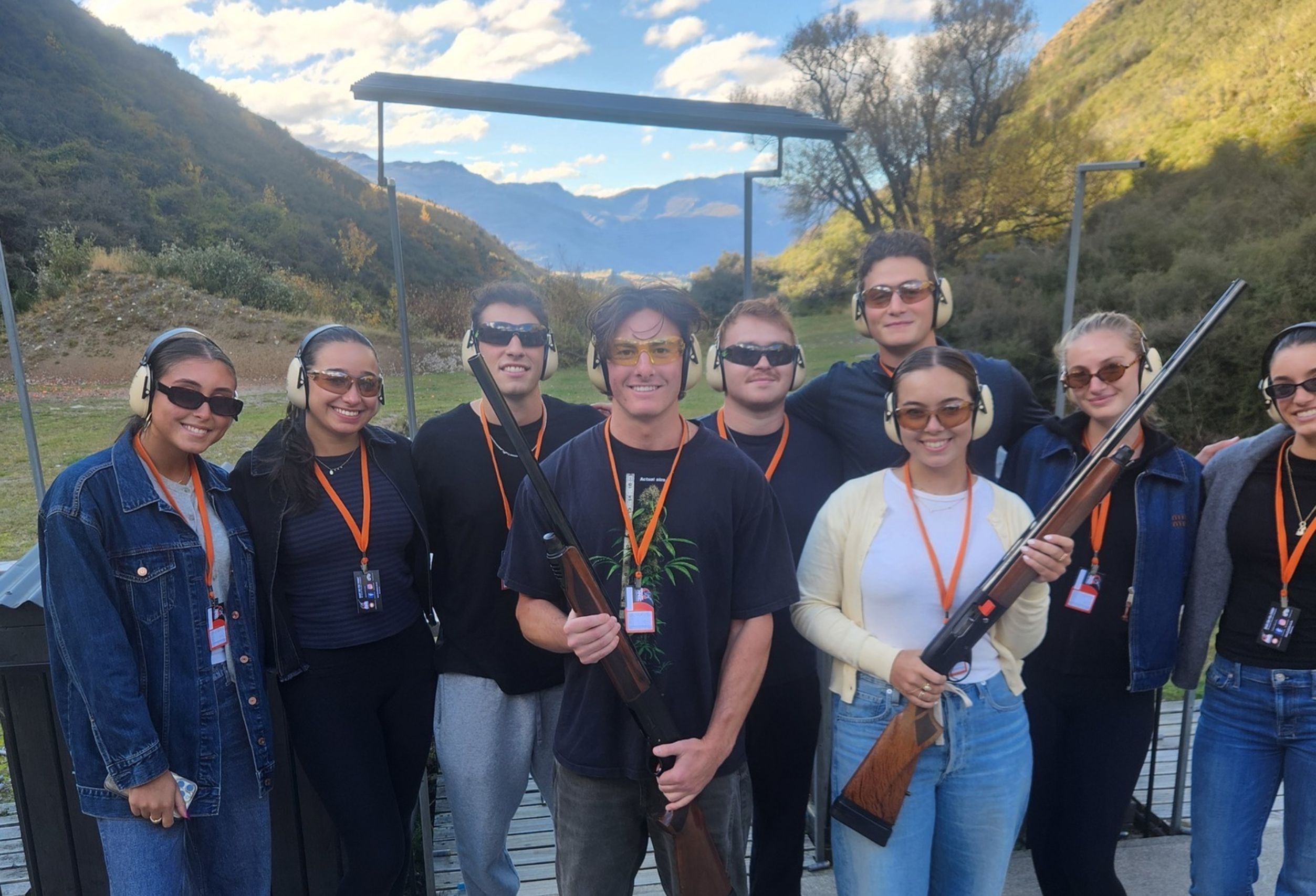 Group of eight friends posing with shotguns after a clay target shooting experience at Break One in Queenstown, smiling and celebrating a fun and supportive session.