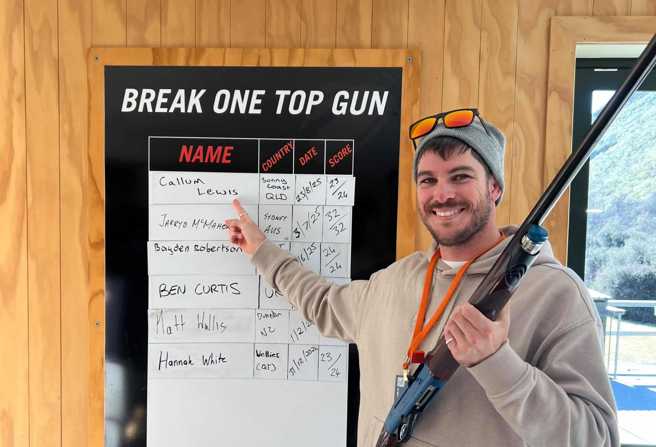 Guest smiling and pointing to his Top Gun scorecard while holding a Beretta shotgun at Break One Clay Target Experience in Queenstown.