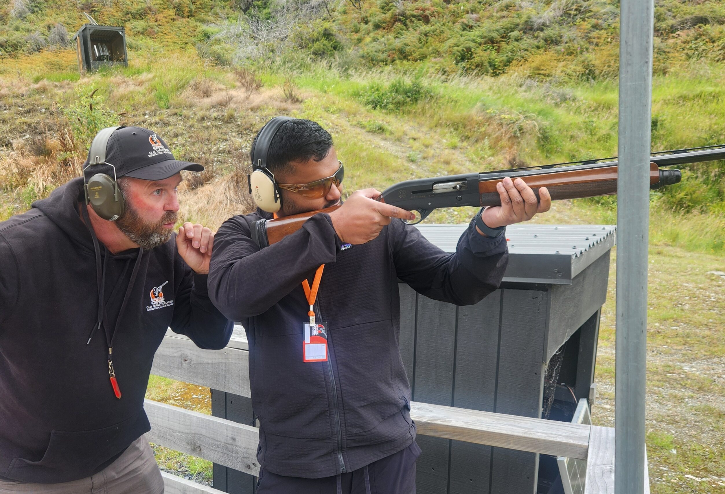 Instructor standing behind a guest, guiding shotgun positioning and targeting during a clay target shooting session at Break One in Queenstown, ensuring a safe and supportive experience.